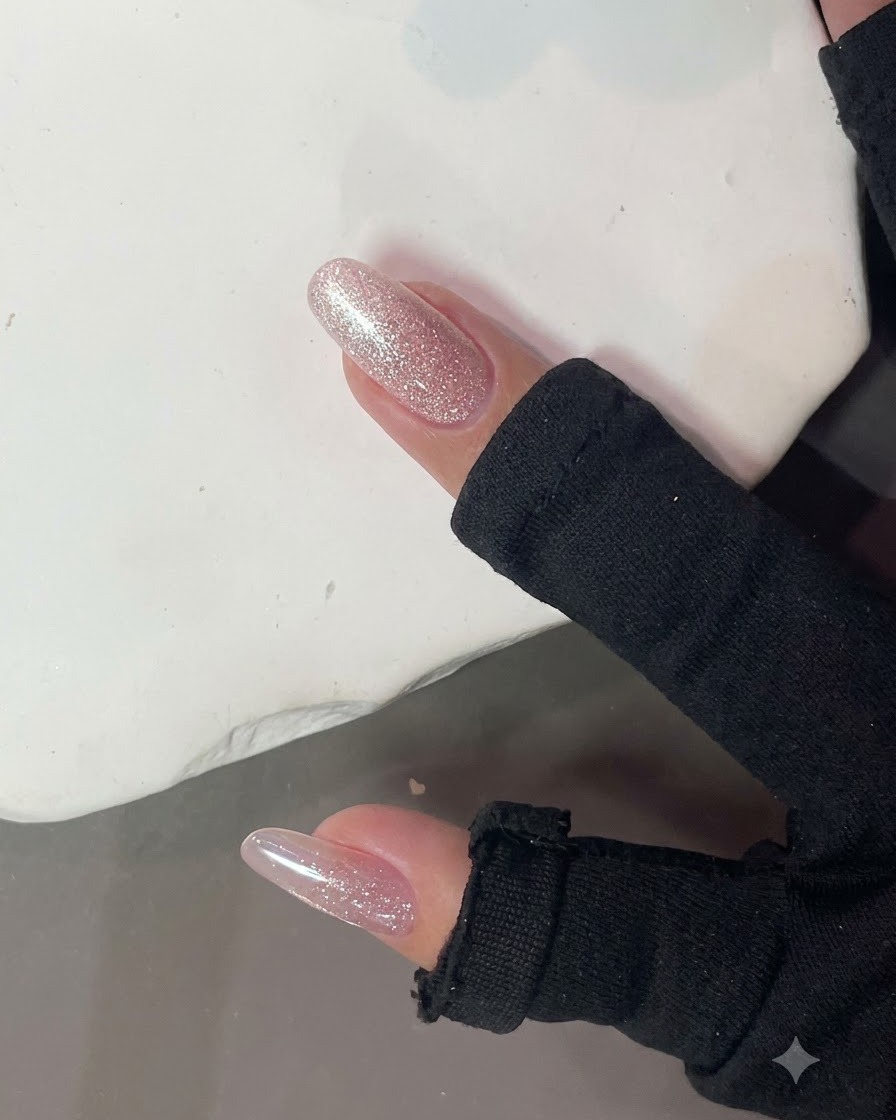 A strong nail magnet held close to a glossy pink glitter nail to form a cat-eye light effect.