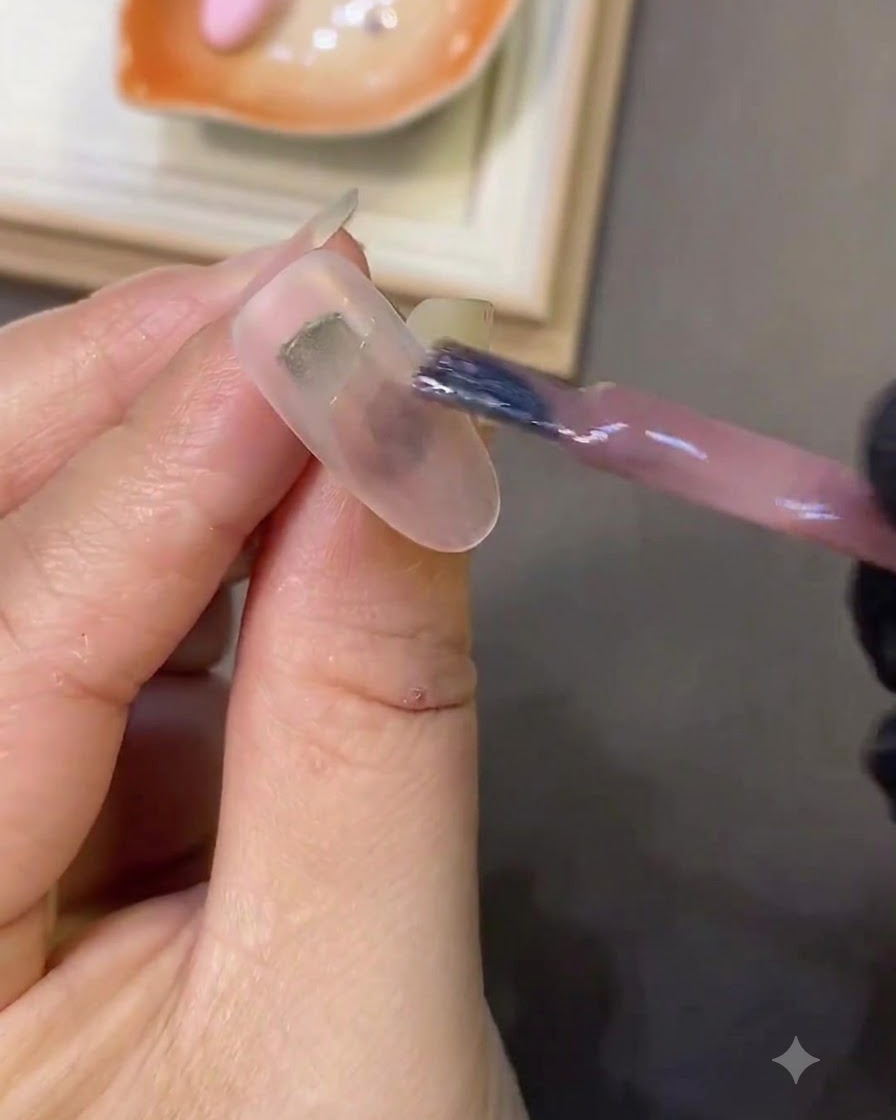 A nail brush applying light pink cat-eye gel onto a milky white nail.