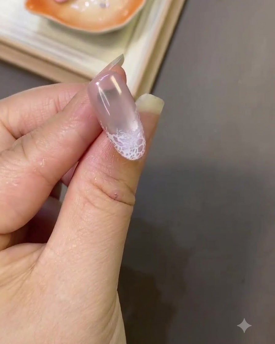 A close-up of a fingernail showing a finished white lace design near the tip with a smooth surface texture.