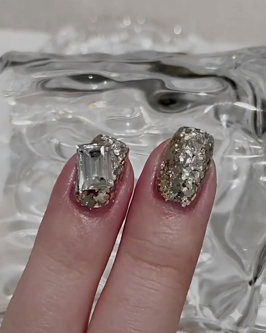 A brush applying a glossy top coat over a glitter nail layer.