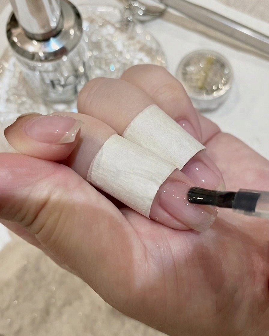 A close-up view of placing a large rectangular crystal onto a nail with adhesive.