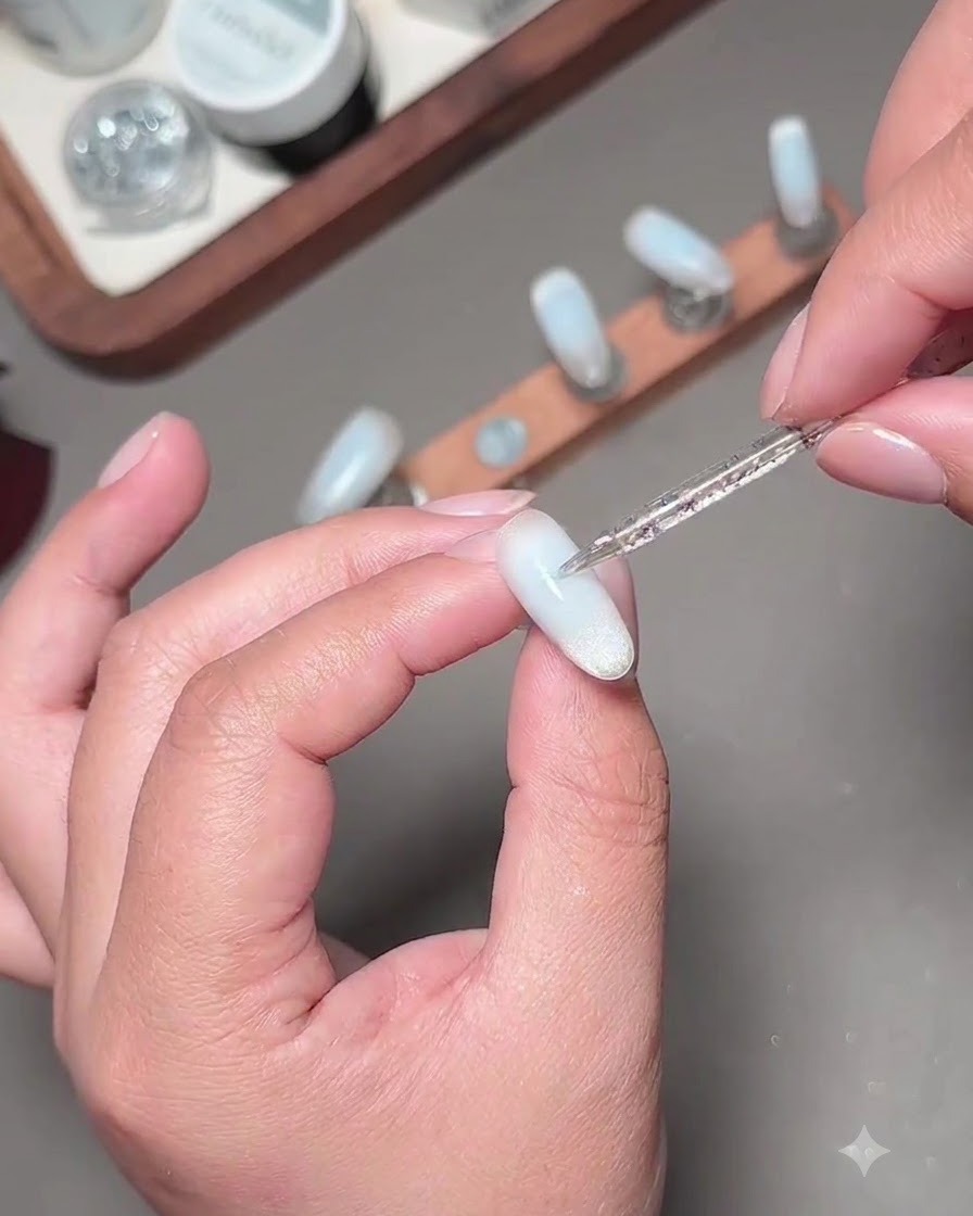 A fine nail art brush applying a second layer of blue gel to darken the center of the nail.