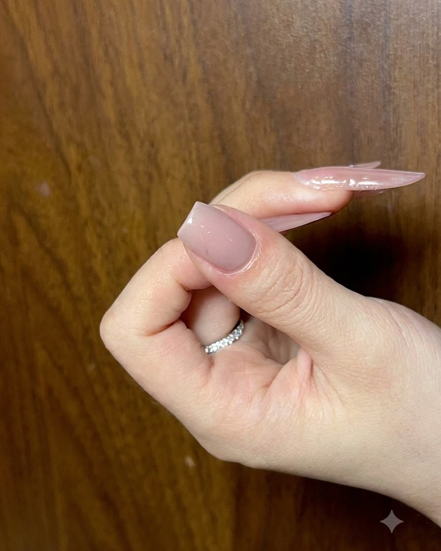 A hand holding a nail with a completed nude base layer, viewed from an angle to check smoothness.