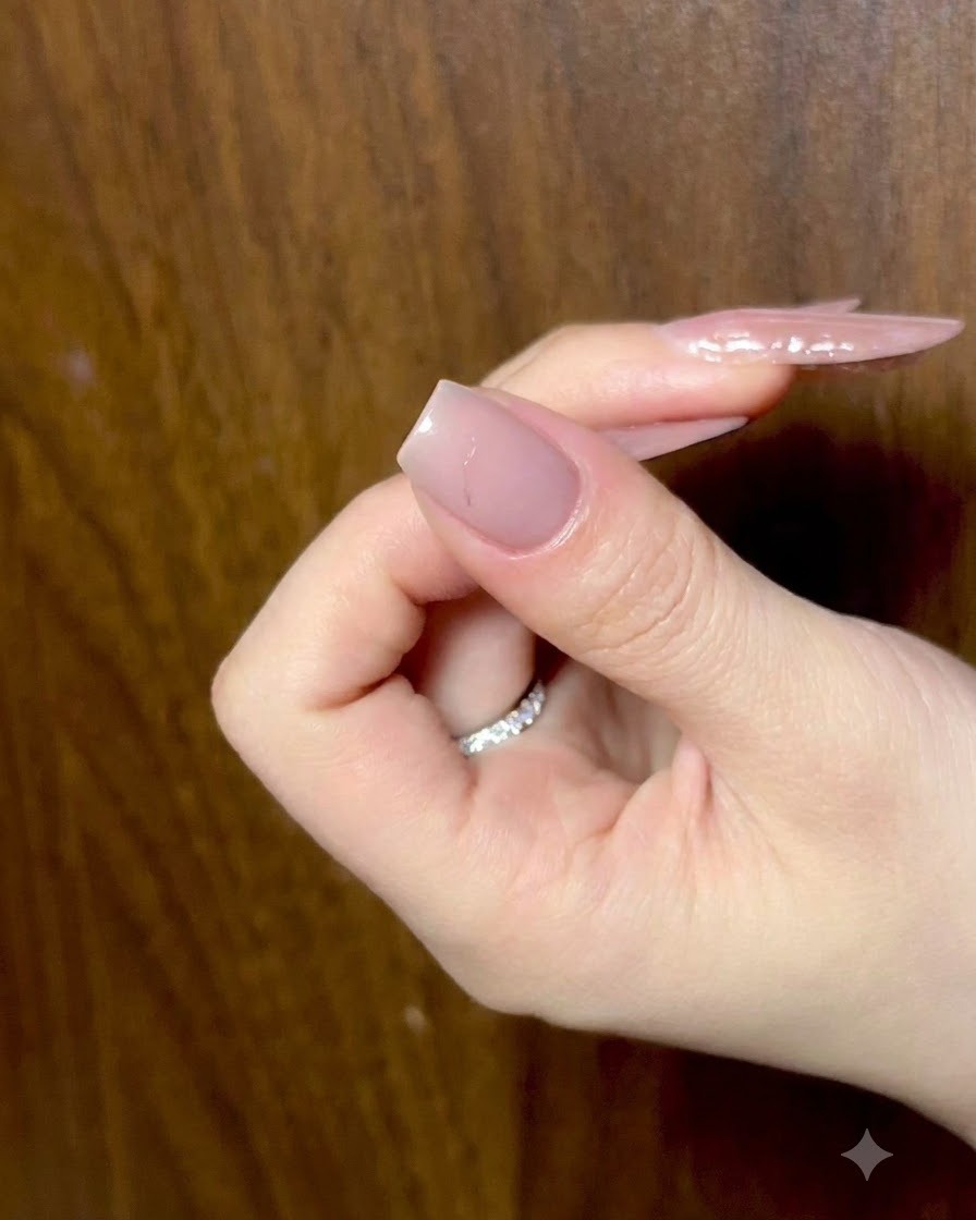 A hand resting with fingers slightly curled, showing prepped nude nails under ambient lighting.