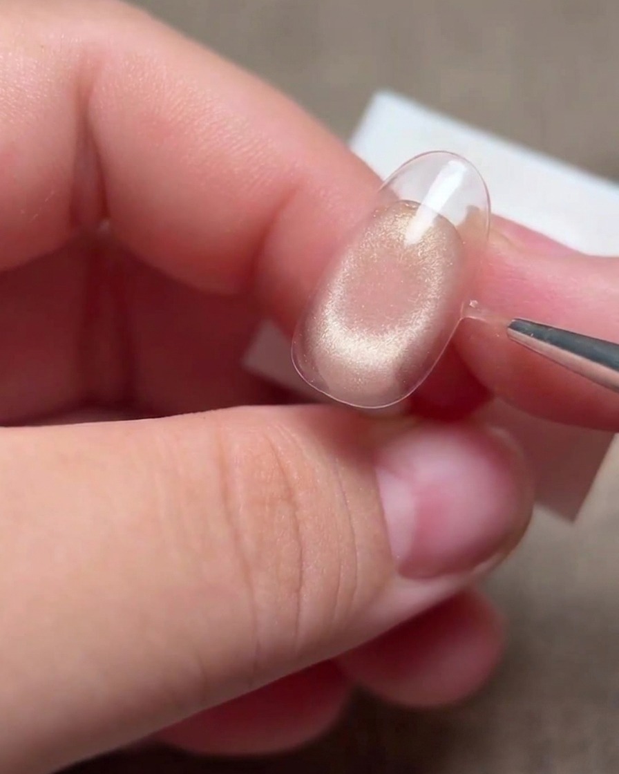 A hand using a thin liner brush to refine the edges of the smile line on a nail tip.