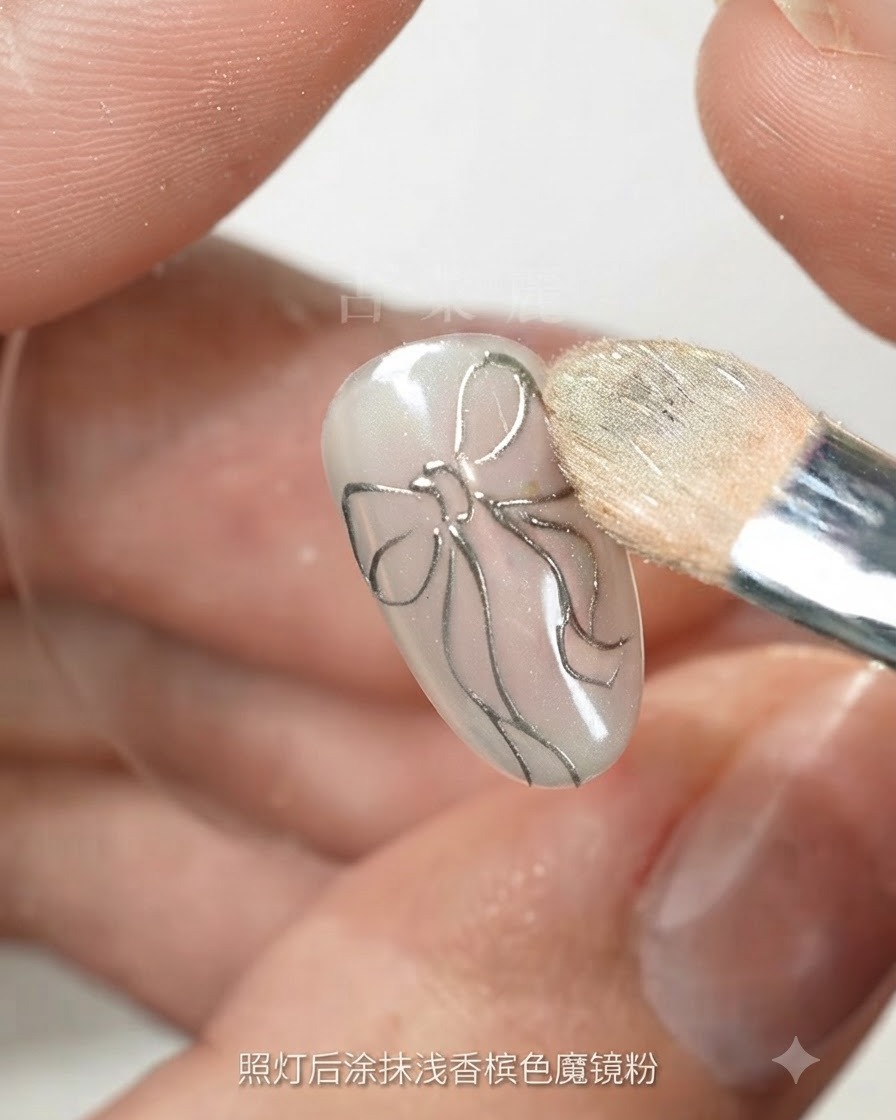 A makeup sponge buffing light champagne magic powder onto a nail with a silver bow outline.