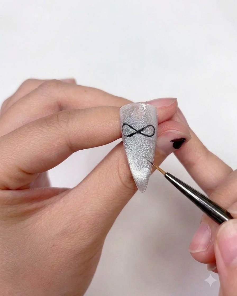A nail artist using a fine liner brush to add two curved ribbon tails extending downwards from the center of the bow art.