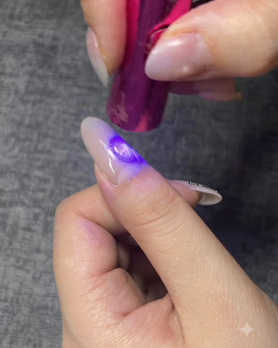 A mini purple UV/LED lamp curing a clear gel layer on a fingernail.