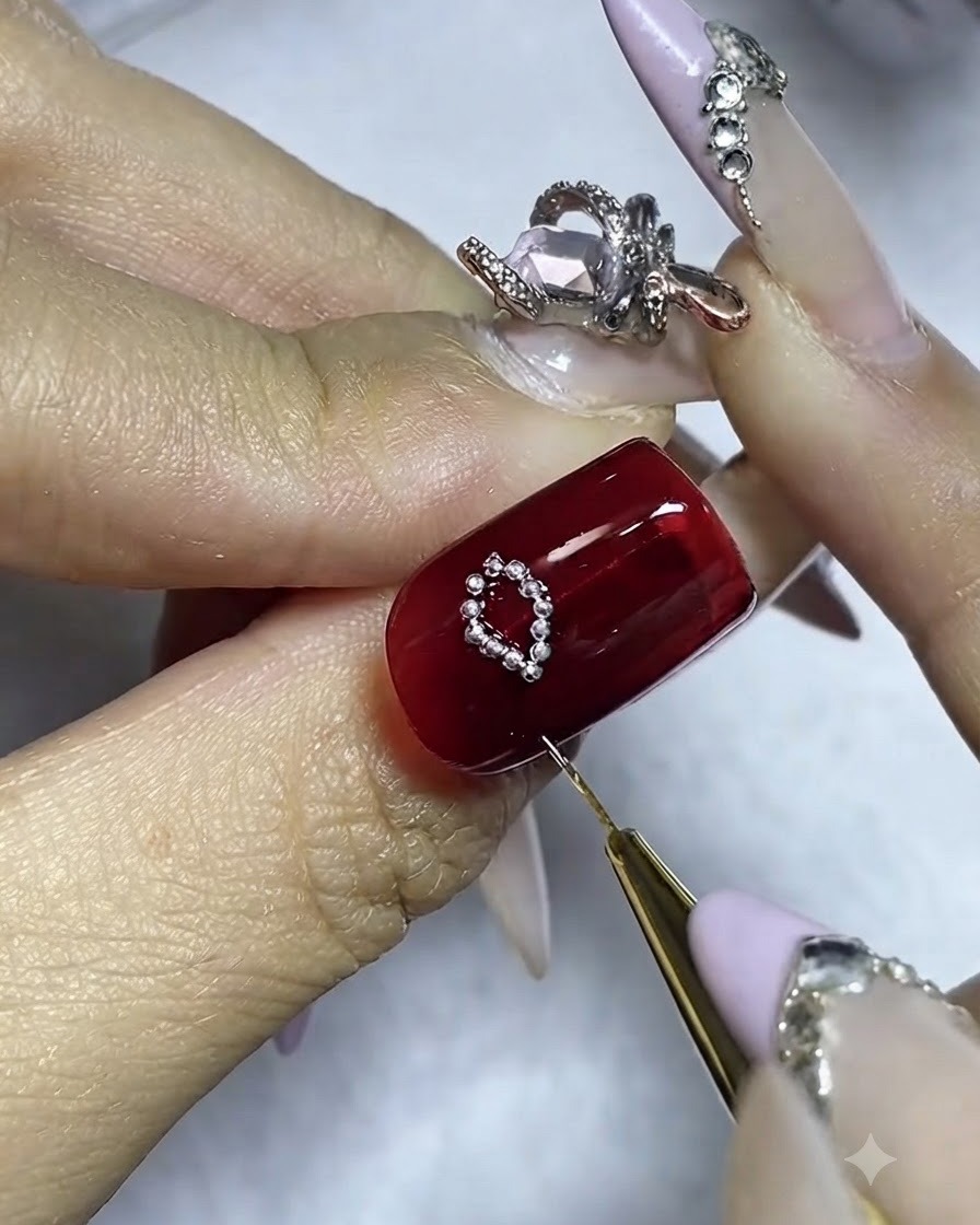 A nail with one complete side of a silver bead bow and glue being applied for the second side.