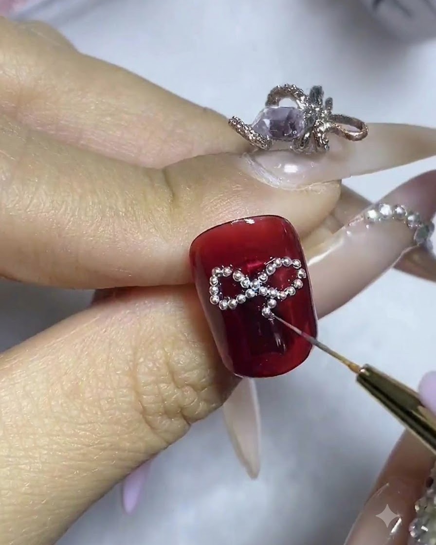 A close-up of a nail showing a central rhinestone being adjusted in the middle of the bead bow framework.