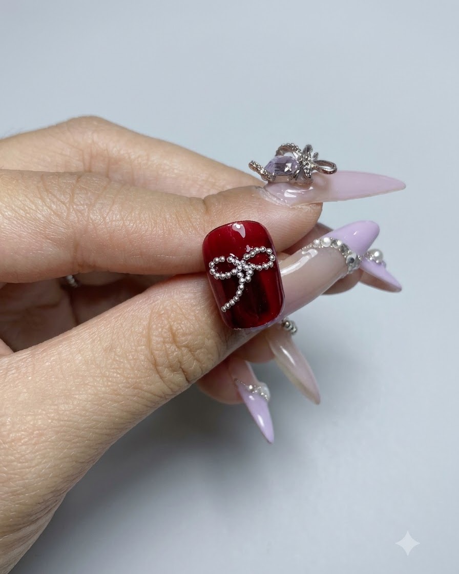 A completed beaded bowknot design on a dark red glossy gel nail surface viewed closely.