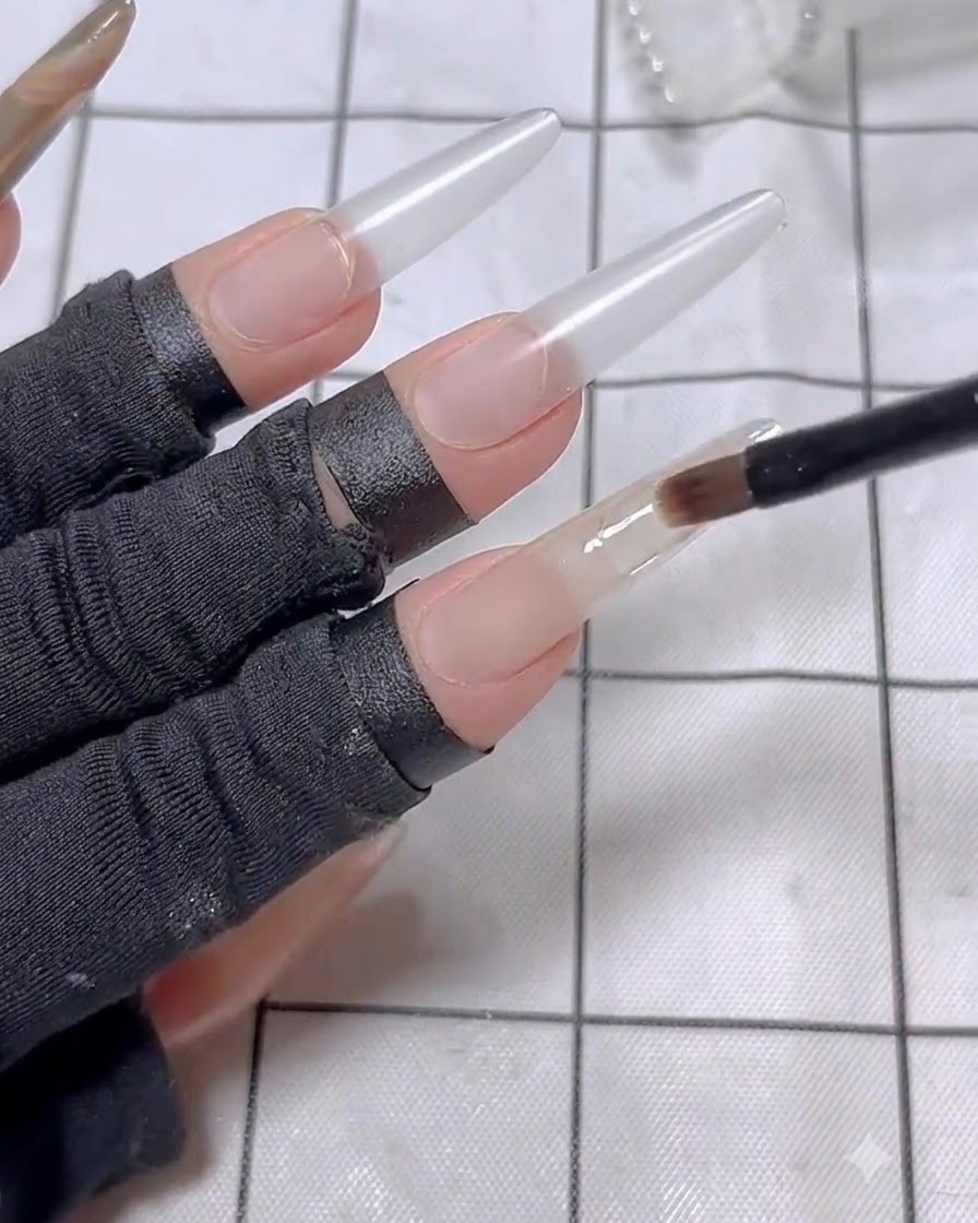 A nail brush applying a second layer of nude base polish onto the index finger.