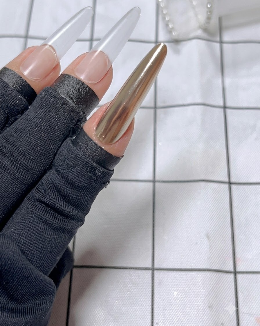 The finished index finger nail featuring a glossy golden mirror surface ready for the ribbon design.