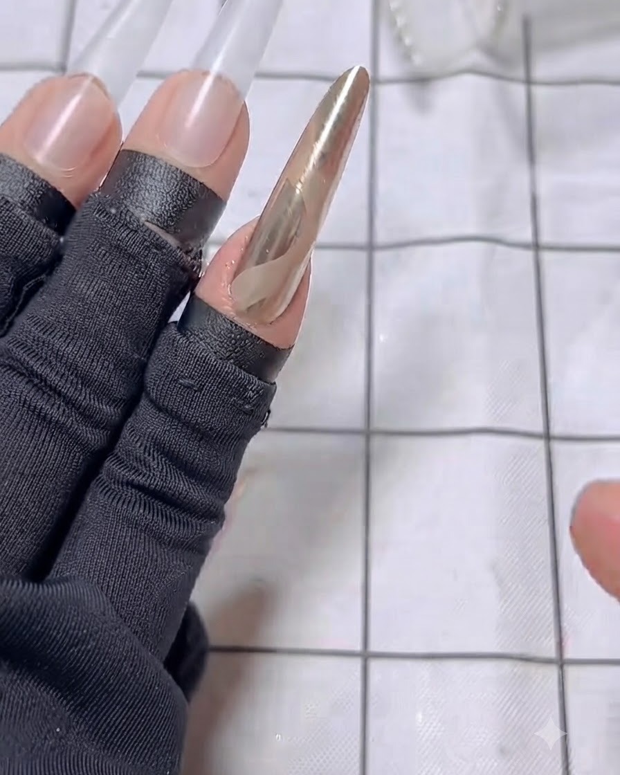 A nail brush applying a coat of nude base polish to a long nail extension on the middle finger.