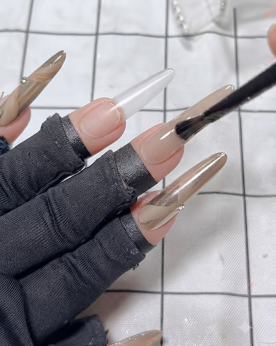 A nail brush smoothing a second coat of nude polish onto the middle finger nail.
