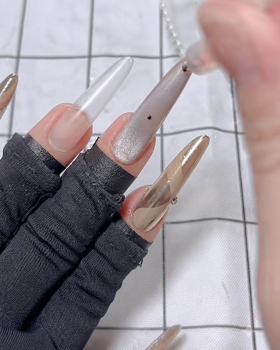 A dotting pen placing small black dots onto the cat eye gel background of the middle finger.