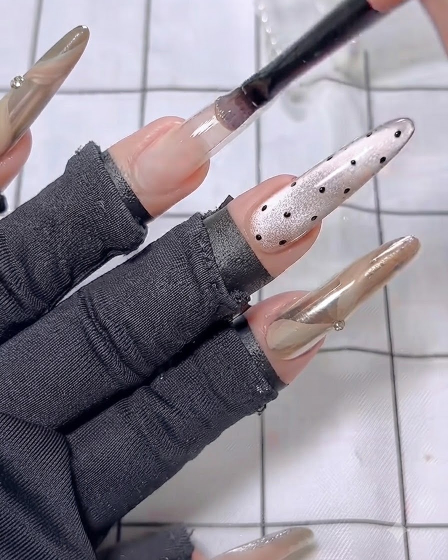 A nail brush applying the first coat of nude polish onto an elongated ring finger extension.