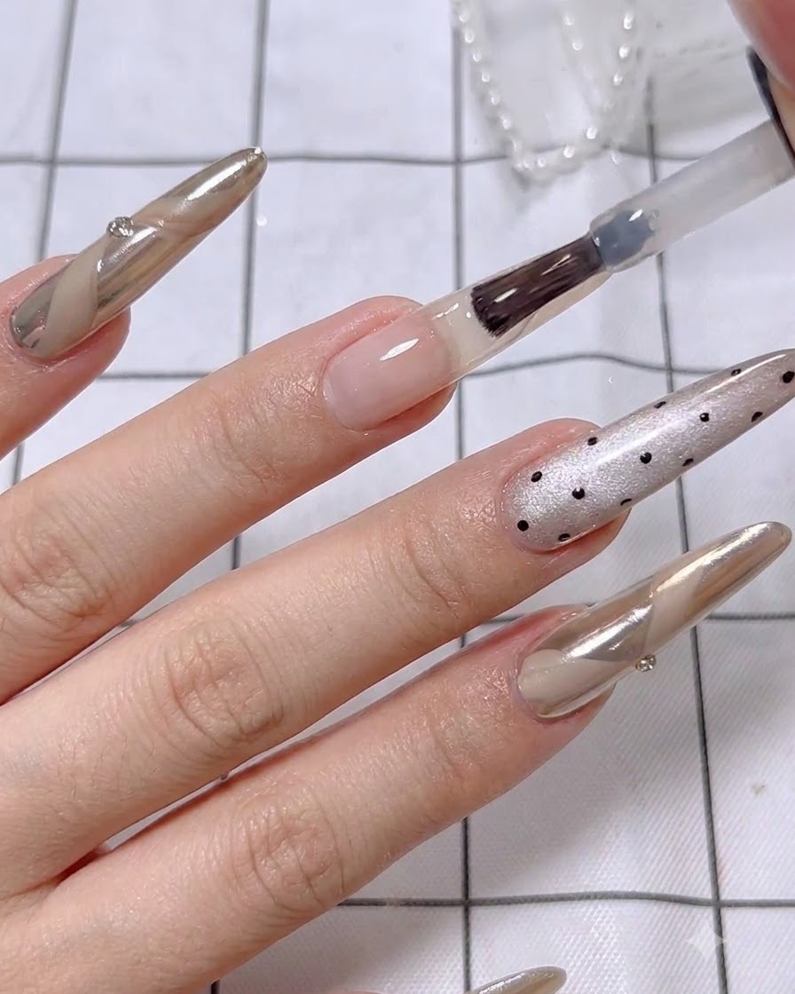 A close-up of a brush applying a second layer of nude base polish on the ring finger.