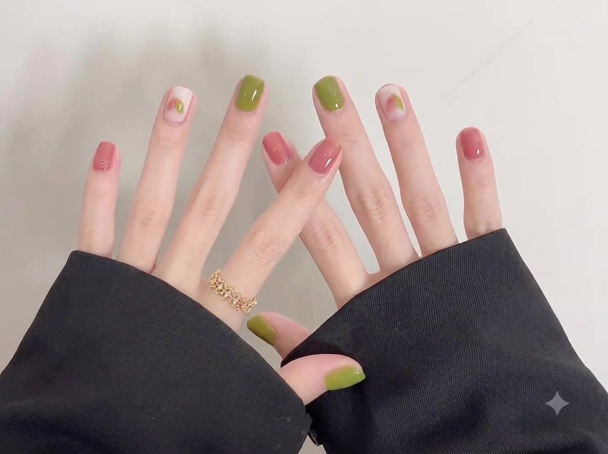 A detailed close-up shot focusing on the right hands glossy green and pink nails with delicate doodle art.