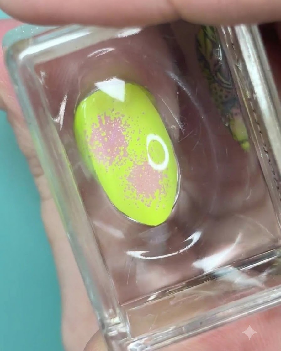 A clear silicone stamper holding a neon green nail with a soft pink gradient and dotted texture.