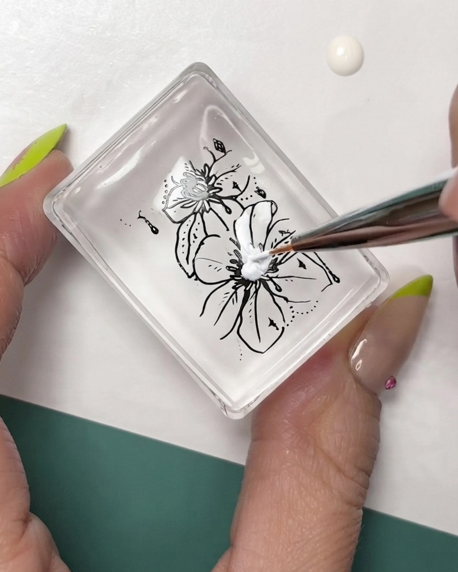 A fine liner brush adding white details to black-outlined floral stamping on a clear stamper pad.