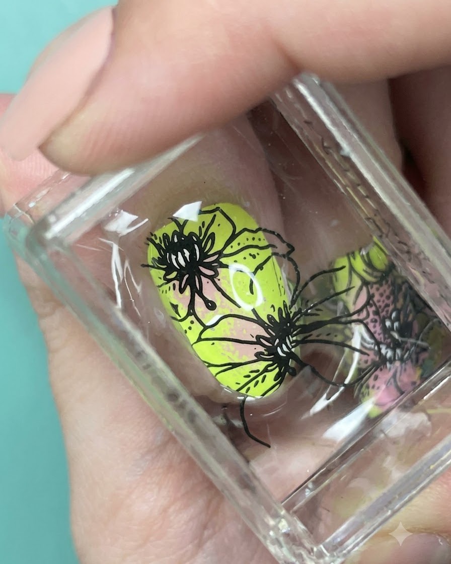 Close-up view of black floral patterns aligned over the neon green and pink gradient nail on a stamper.