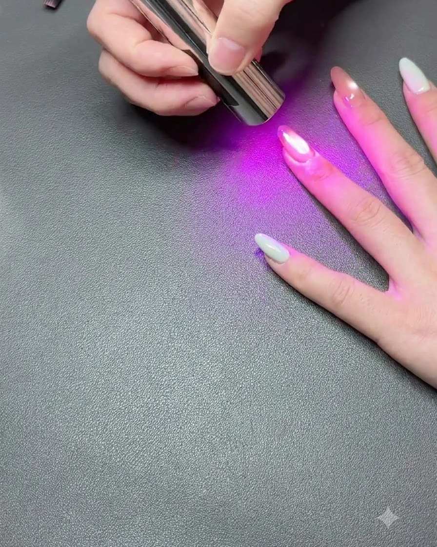 A hand resting on a dark surface while a portable UV lamp cures the cat-eye gel polish.