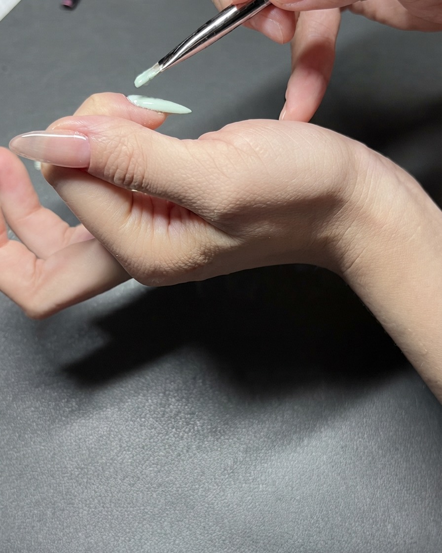 A detail view of a nail brush applying mint green gel polish precisely onto an index fingernail.