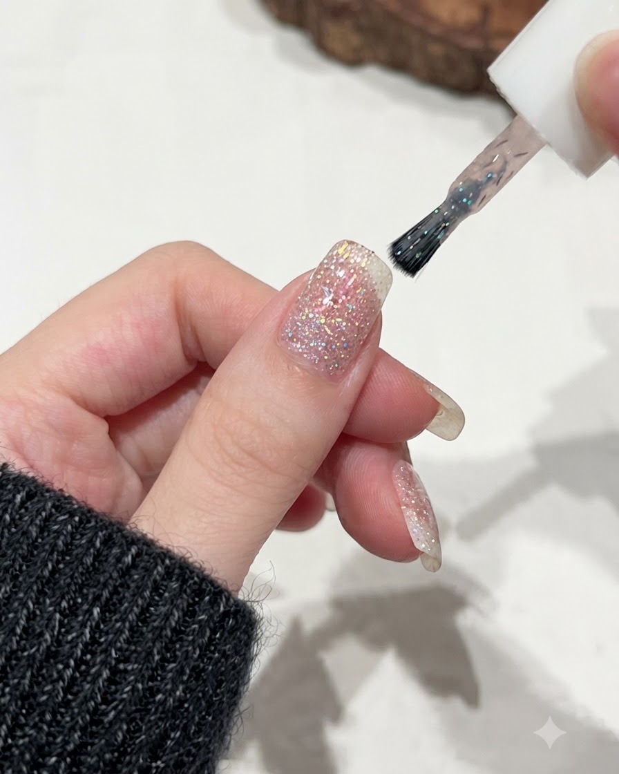 A brush applying C62 shimmer and glitter gel coat over a pink glitter nail base.