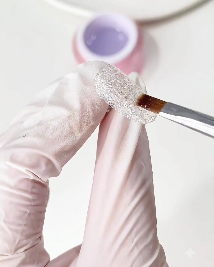 A brush applying a clear layer of base gel over the sparkling crushed diamond nail base.