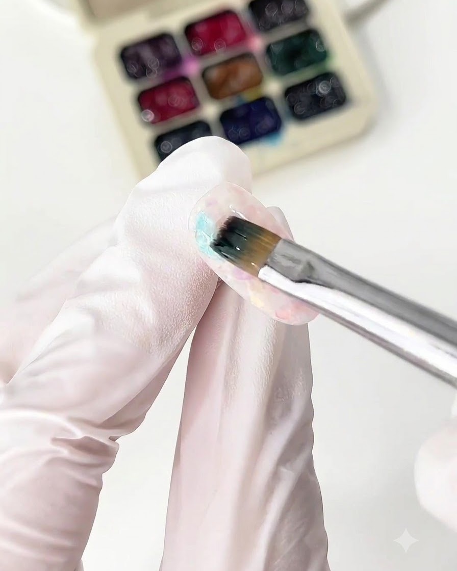 A fine brush applying blue glass gel onto a nail tip.