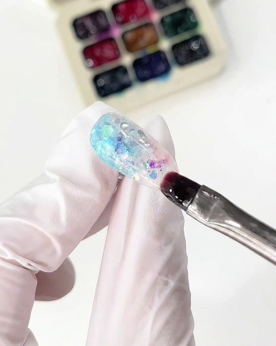 A fine brush applying pink glass gel next to the blue section on a nail.