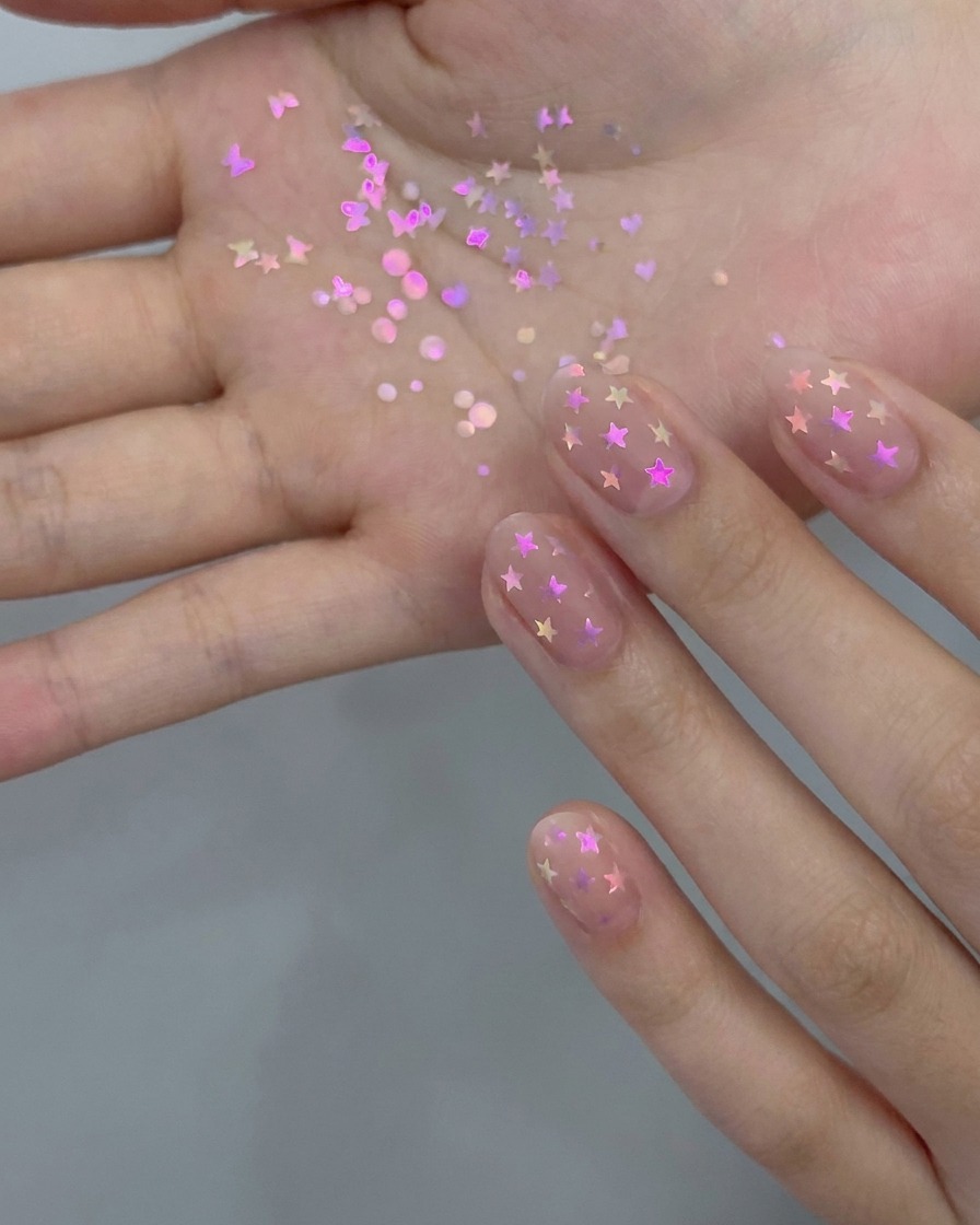 A manicure brush applying a thin layer of sheer nude gel polish onto a natural fingernail.