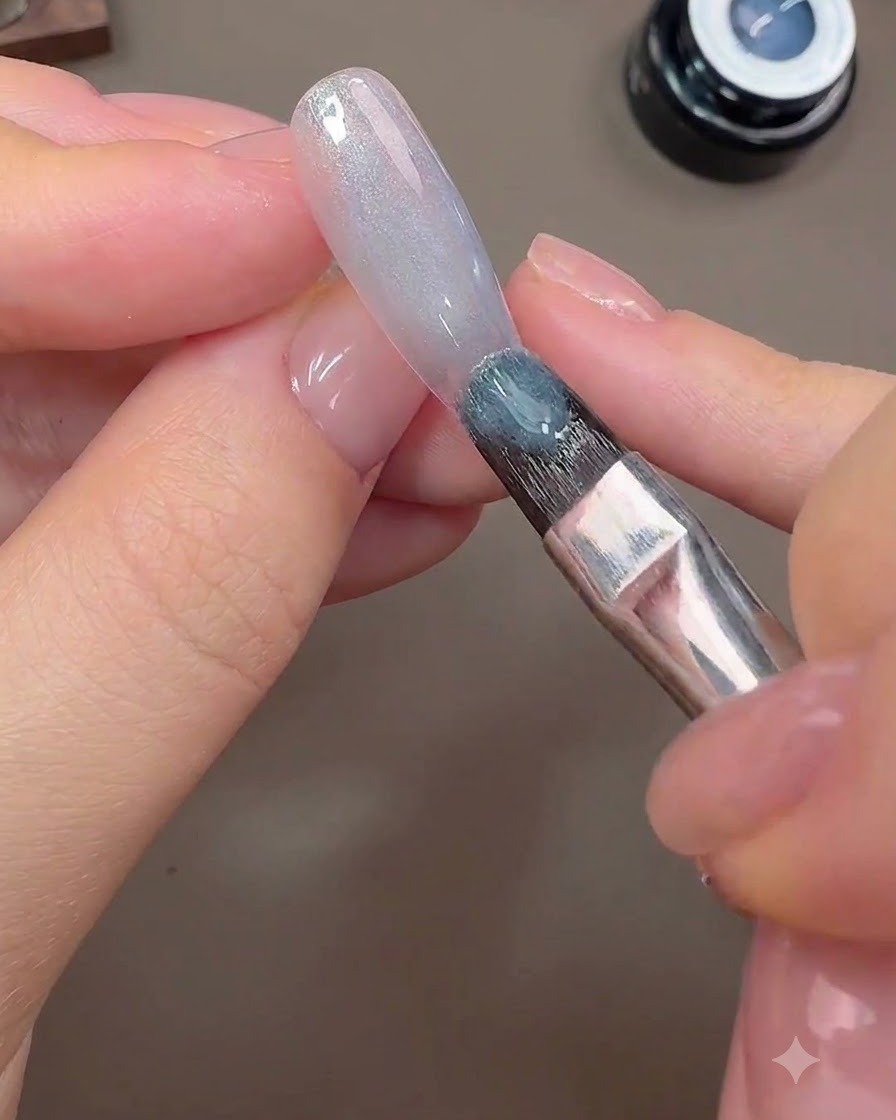 A brush applying gray-blue cat-eye gel onto the nail surface to form the galactic background.