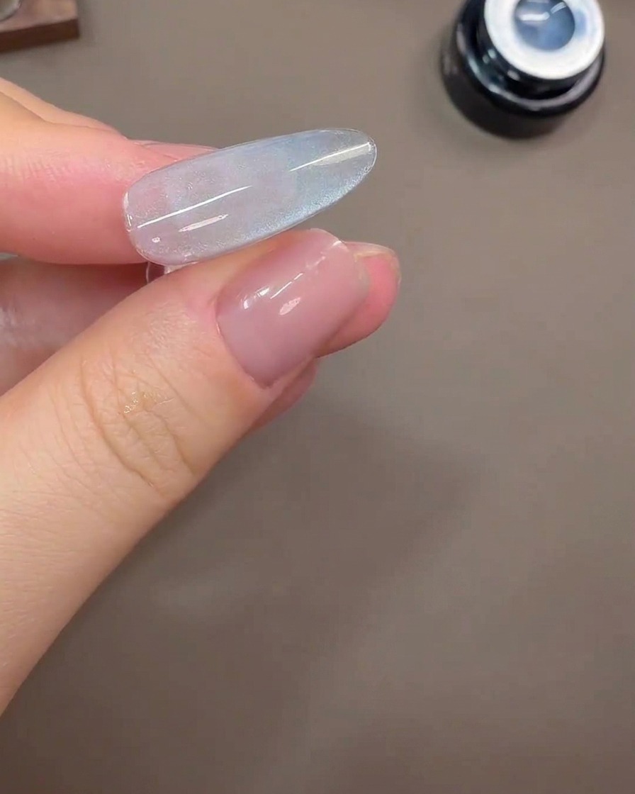 A nail showing a wide cat-eye light reflection on a gray-blue gel background.