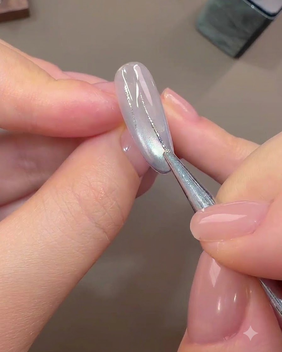 A fine nail art brush drawing thin abstract lines with silver foil gel over a light-colored cured base nail.