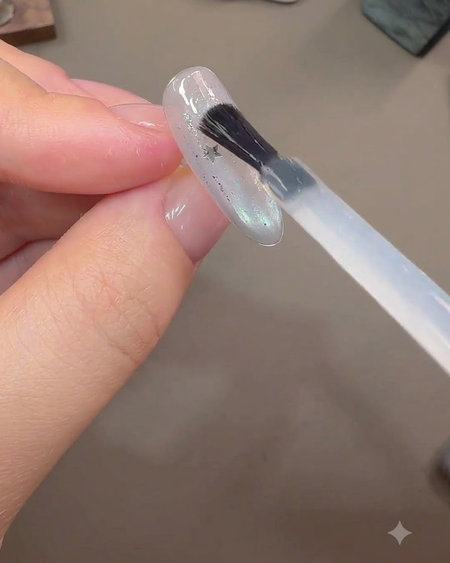 A brush applying a thick layer of builder gel over embedded star glitter pieces on a finished nail extension.