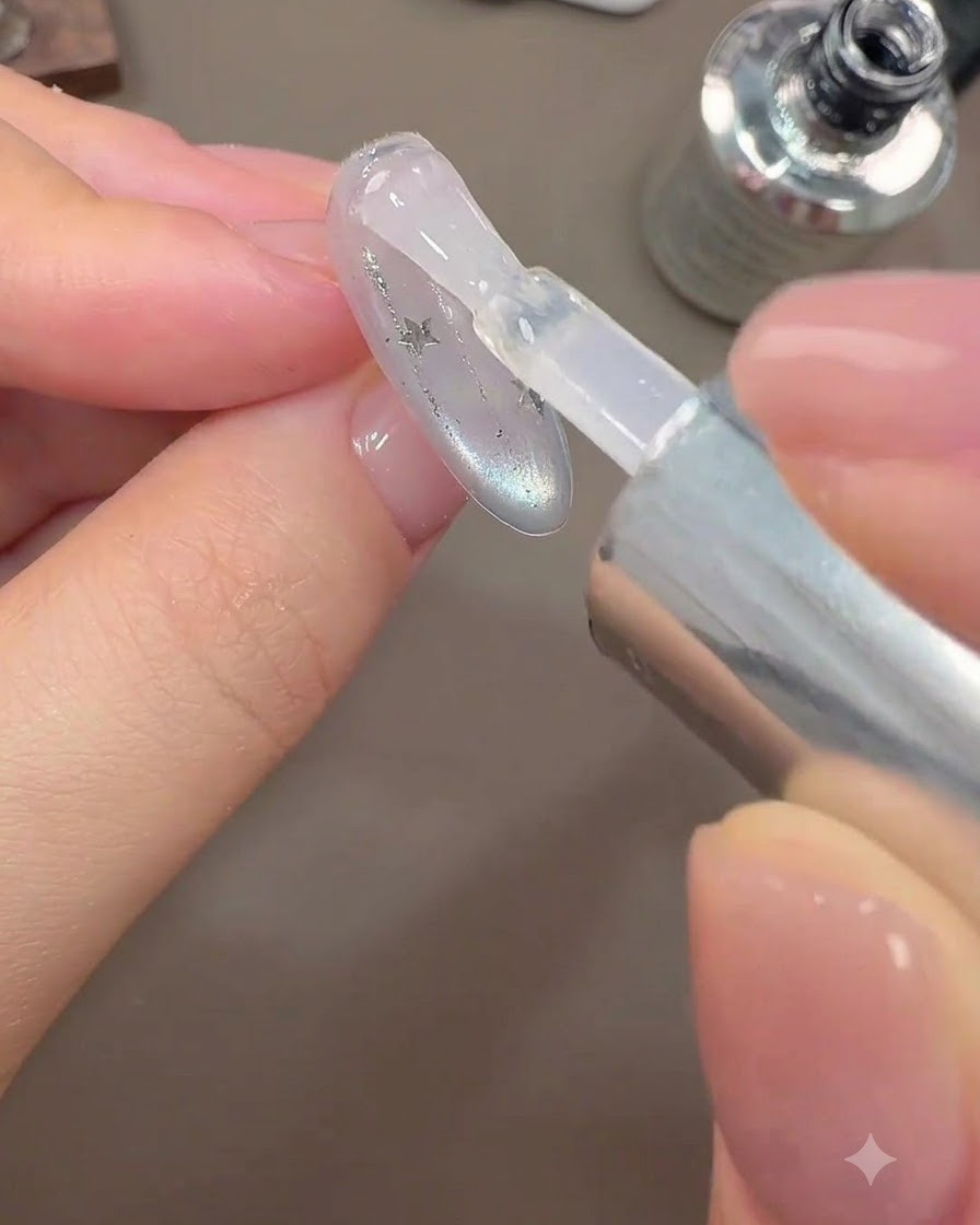 A brush applying a final glossy top coat layer onto a galaxy nail design.