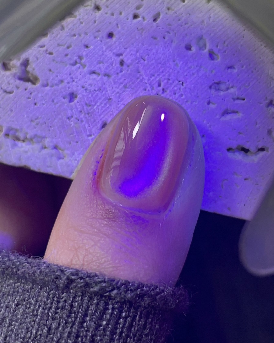 A fingernail curing underneath a purple UV/LED mini lamp.