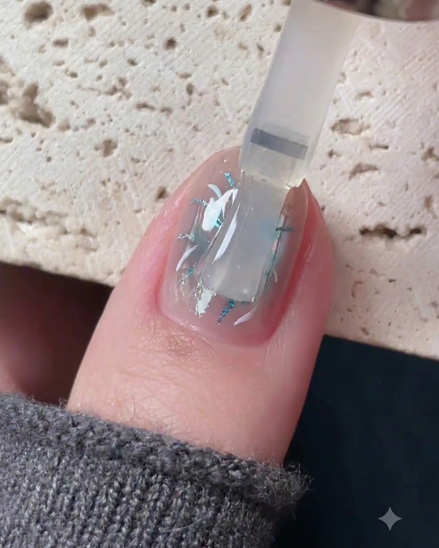 A brush applying a clear self-leveling top coat over a detailed nail art design.
