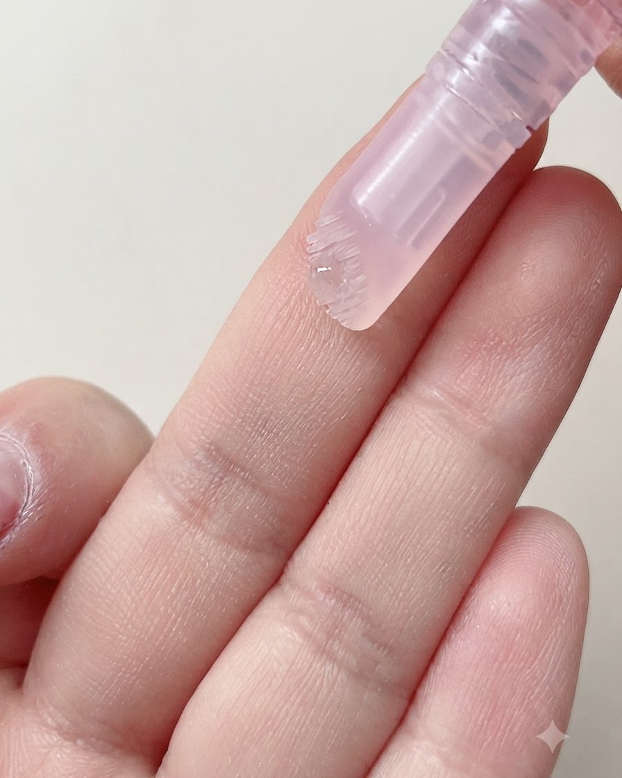 A soft brush head of a cuticle pen dispensing a drop of moisturizing serum onto a finger.