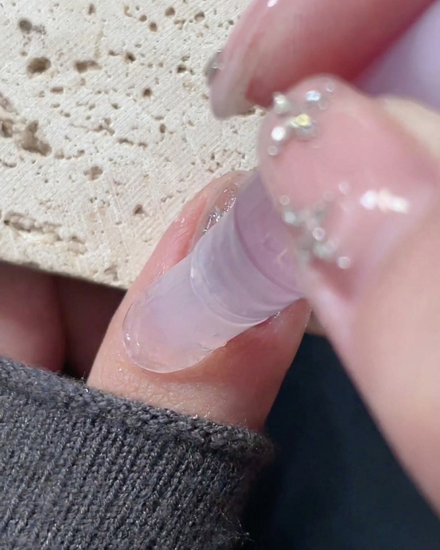 A cuticle oil pen being applied around the edge of a finished nail to moisturize the skin.