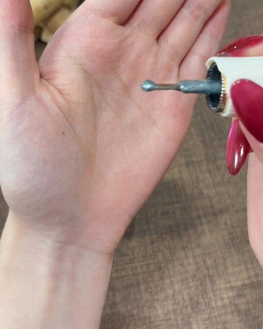 A close-up view of a brush tip holding a small rounded bead of greyish gel polish.