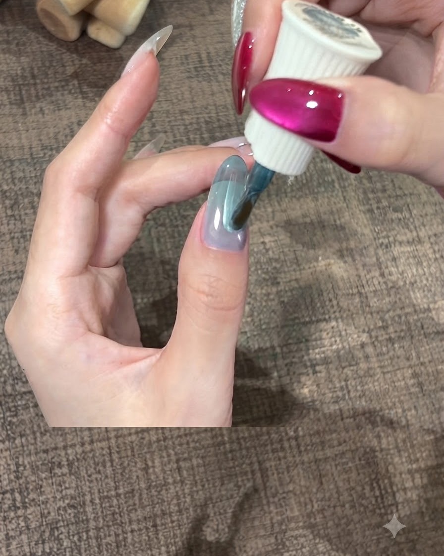 A brush spreading a thick layer of teal gel polish smoothly over a thumb nail.