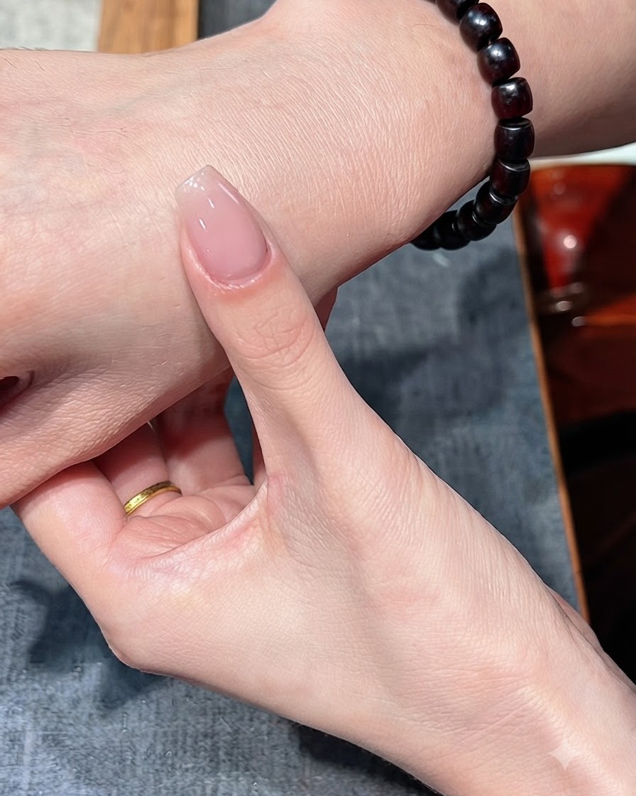 A fingernail with a single coat of nude polish held against the back of the hand.
