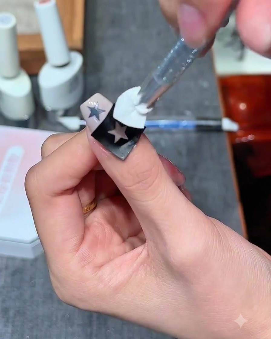 A sponge stamp applying milky white gel over a hollow star sticker on a nail.