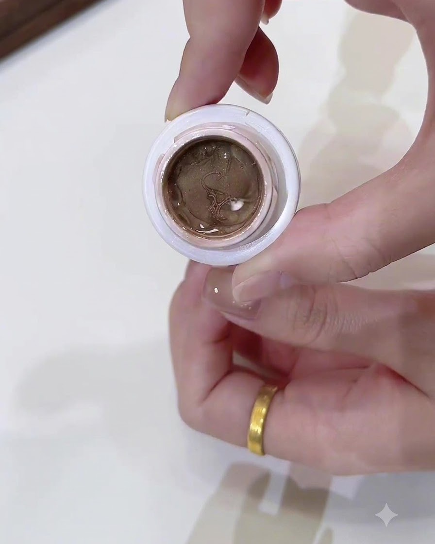 A close-up of a small open jar filled with dark champagne gold cat eye gel held by a hand.