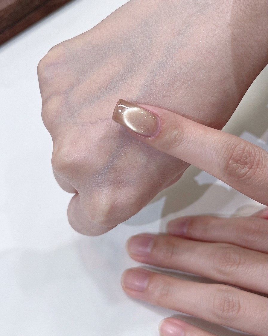 A hand holding a magnet swirling above a champagne gold cat-eye nail to form a flowing light effect.
