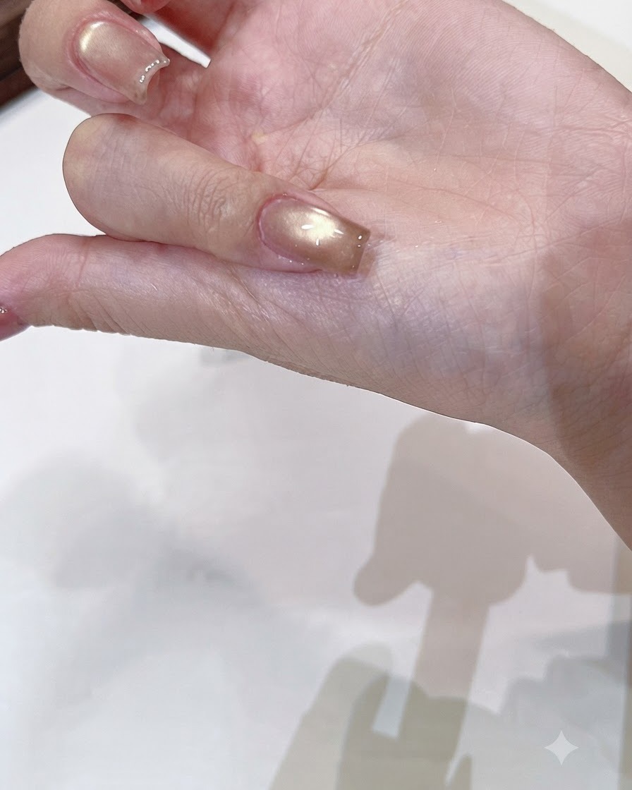 A brush applying a clear shiny top coat over a cured champagne gold cat-eye nail.