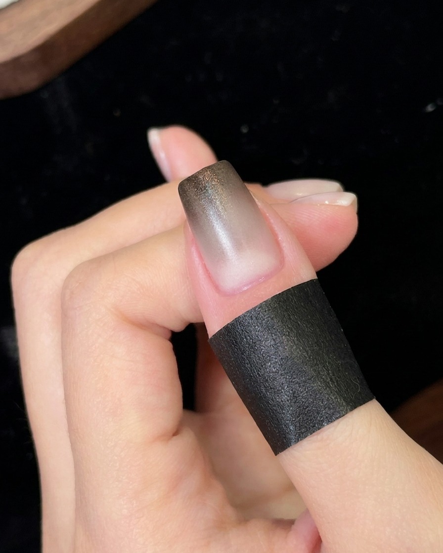 A nail positioned under a small portable UV/LED lamp curing the newly applied black gradient layer.